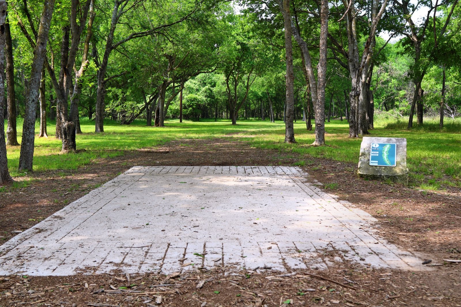 Concrete tee pad and hole sign on a tree-lined fairway at the Roy G. Guerrero disc golf course