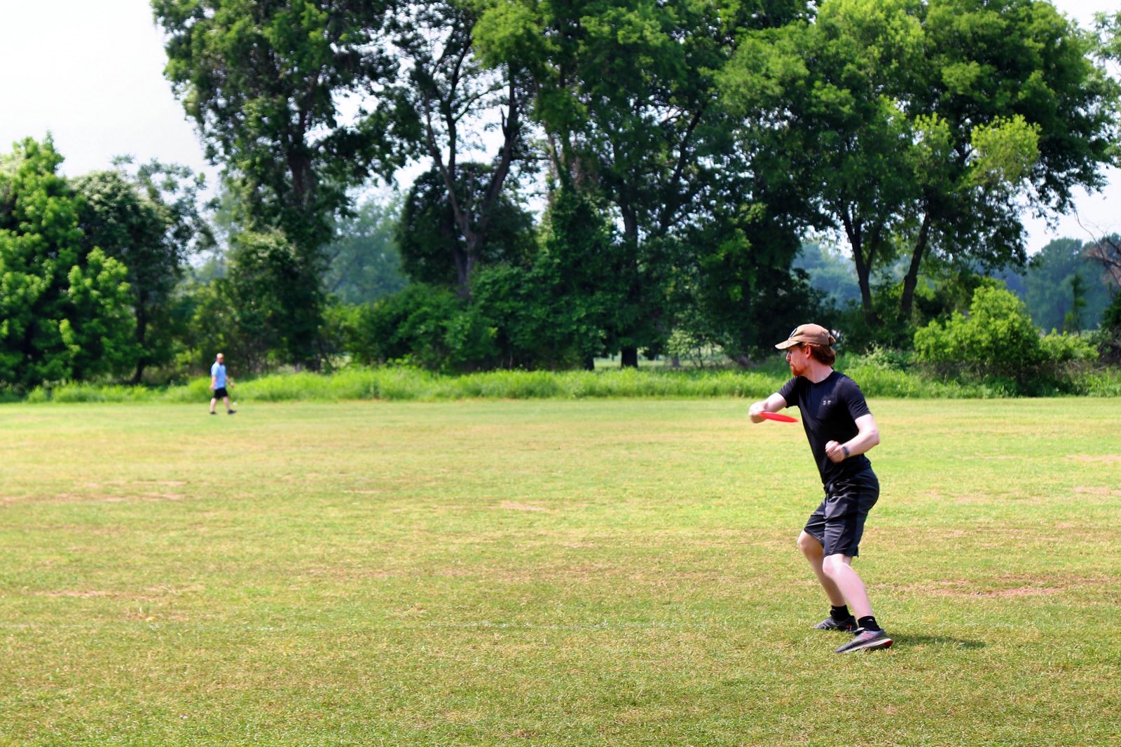 A player throwing a disc across an open grassy field at Roy G. Guerrero park